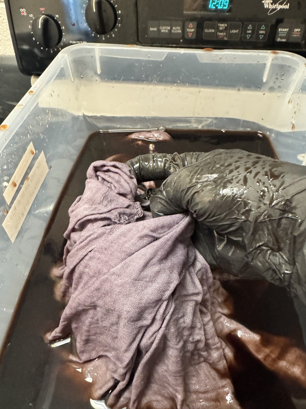 Double gauze soaking in a tub of dark dye, lifted with a gloved hand